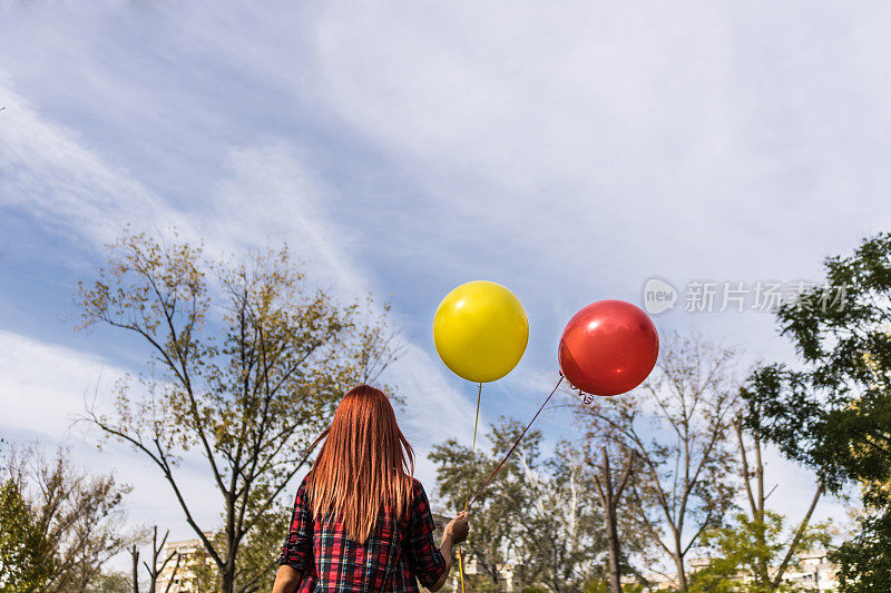 后视图的女人与气球走过公园。