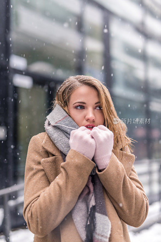 一个年轻女子在一个下雪的冬日在城市里取暖。