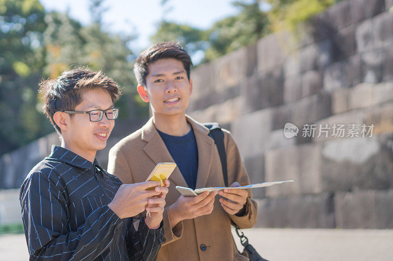 年轻的亚洲男子和日本朋友寻找旅游地点使用手机和花时间在亚洲旅行