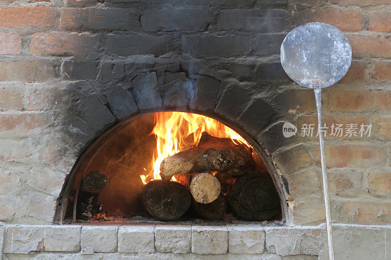 法师传统的户外砖砌披萨炉，木材燃烧炉意大利餐厅的披萨用燃烧的原木和土地处理，金属披萨桨铲