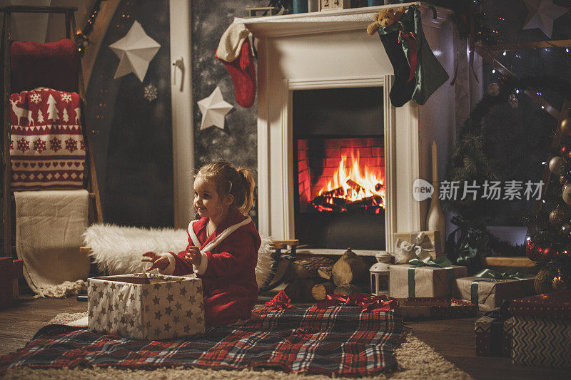 可爱的小女孩坐在壁炉旁，打开她的圣诞礼物