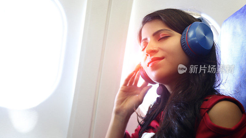 年轻女性在空中旅行时戴着音乐耳机放松