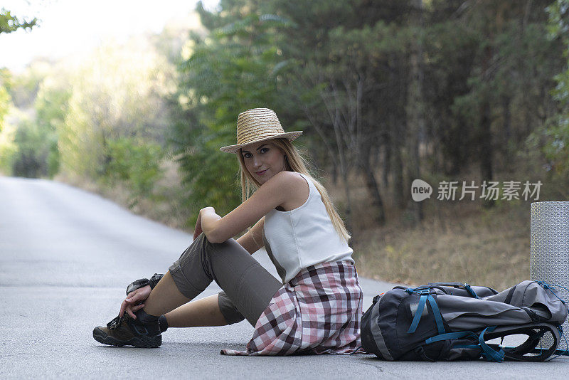 女旅人坐在路上，望着别处的路。背包徒步者在路上放松，欣赏日落