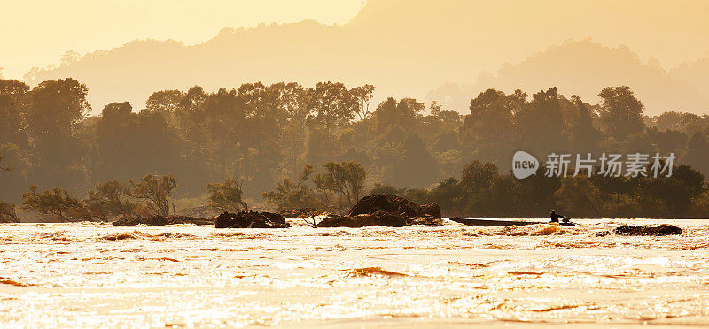 黄昏时分，一名老挝渔民驾着一艘木船穿过湄公河上的急流。