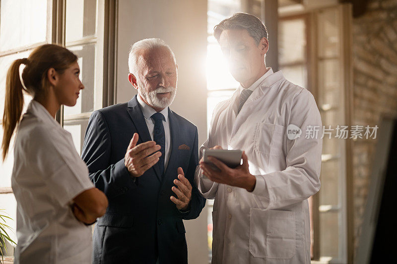 资深商人和医生在诊所触摸板工作时合作。