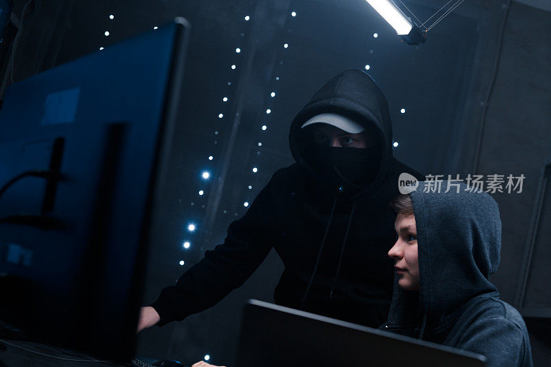 两名黑客看着监视器，讨论用来破坏安全系统的新软件代码。