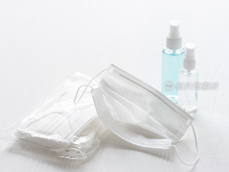 外科口罩，旁边是一包口罩和两瓶洗手液，在白色的桌子背景上，选择聚焦，聚焦在前景的口罩上。