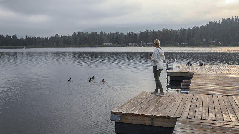 成熟的女人在湖边喝着热饮放松