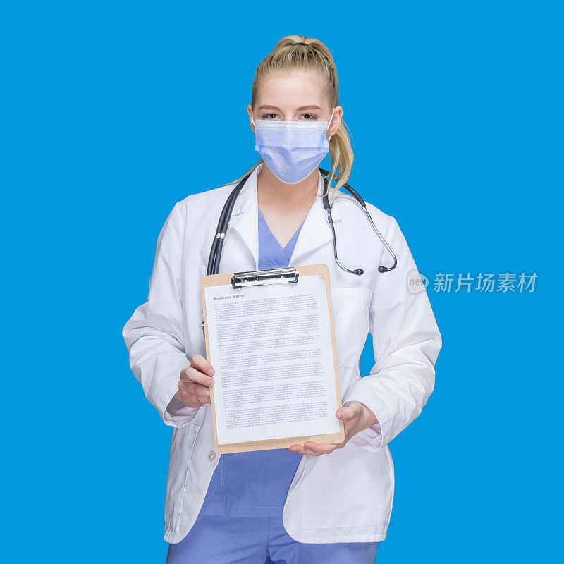 白种人年轻女医生站在蓝色背景下穿着实验服拿着写字板