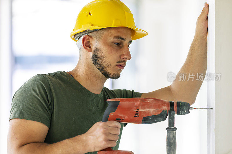 建筑工人用无绳钻在翻新房屋的墙壁上钻孔