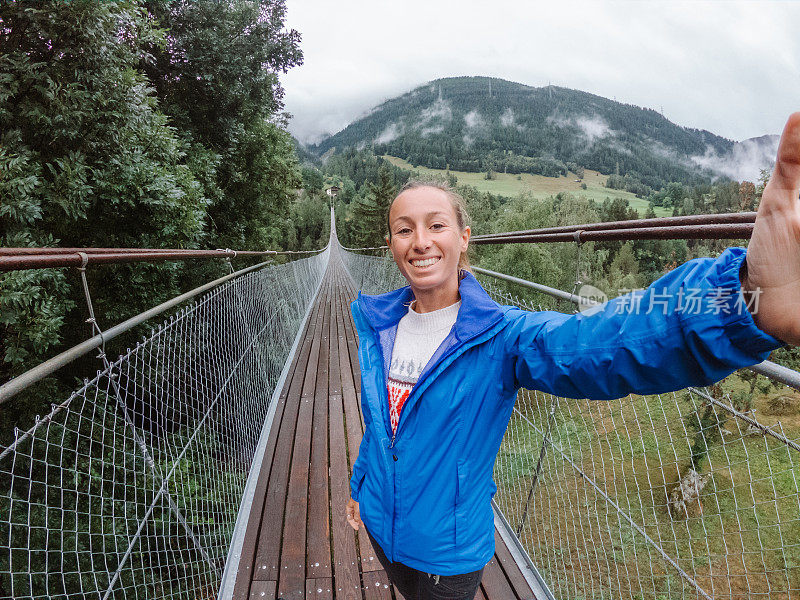 一名女子在穿过松树谷的吊桥上自拍
