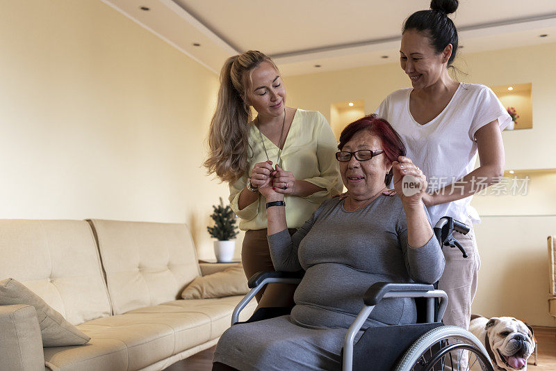 坐在轮椅上的老年妇女正在接受她的细心女儿在家里的帮助。