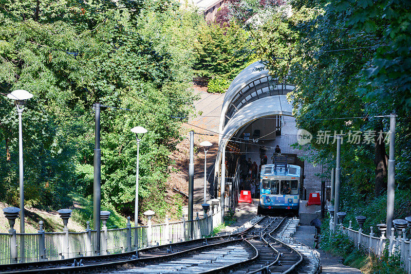蓝色和白色的缆索在较低的车站搭载乘客，周围是夏季的绿色公园。