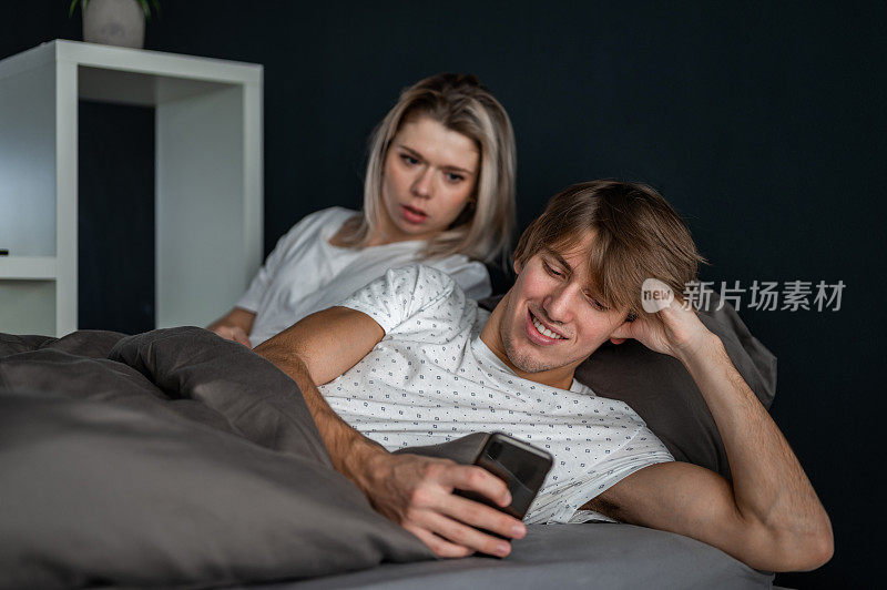 一对年轻夫妇躺在床上玩手机
