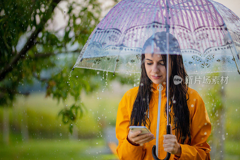 穿着黄色雨衣的年轻女子在雨中使用手机