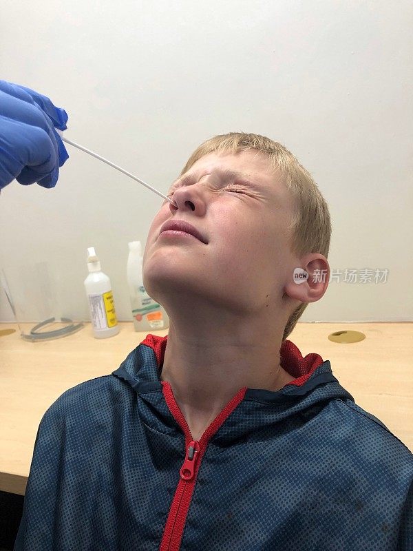 在实验室对一名男孩进行COVID-19鼻拭子检测，显示疼痛