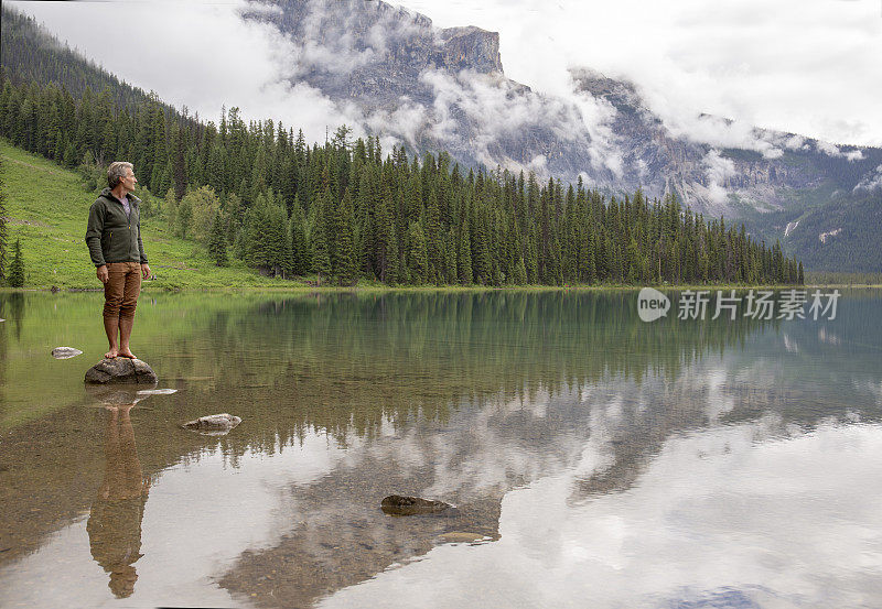 一名男子在暴风雨天站在高山湖中的岩石上