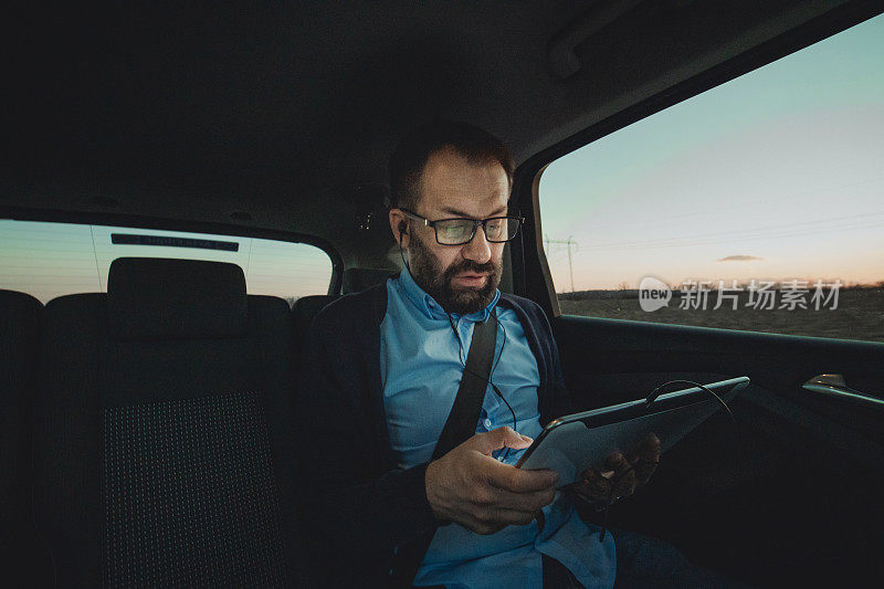 商人在汽车上使用平板电脑。一个商人坐在一辆豪华轿车的后座上，这是一次商务旅行