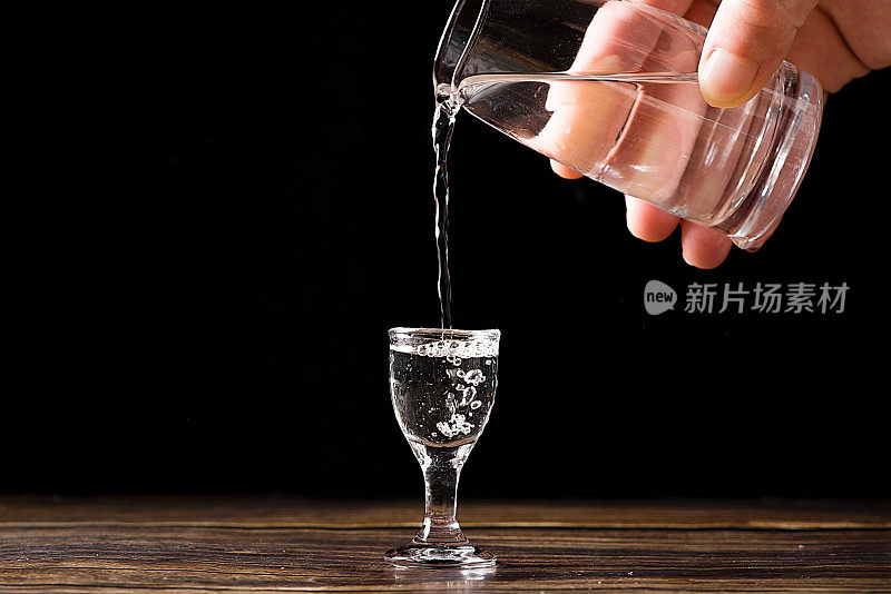 中国白酒，烈酒饮料从一个瓶子倒进一个玻璃杯的木材背景