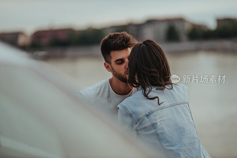 一对相爱的年轻情侣坐在河岸上接吻