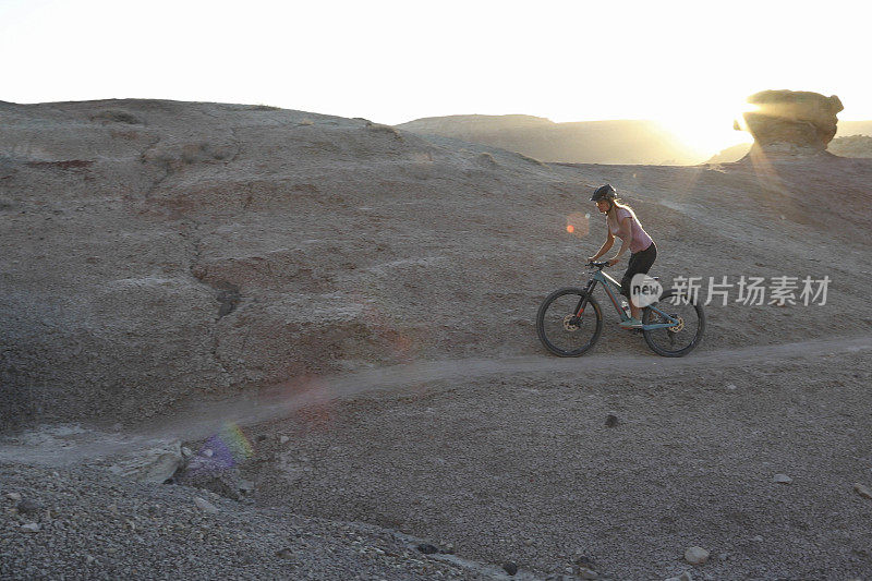 日出时，女山地自行车手沿着沙漠小径骑行