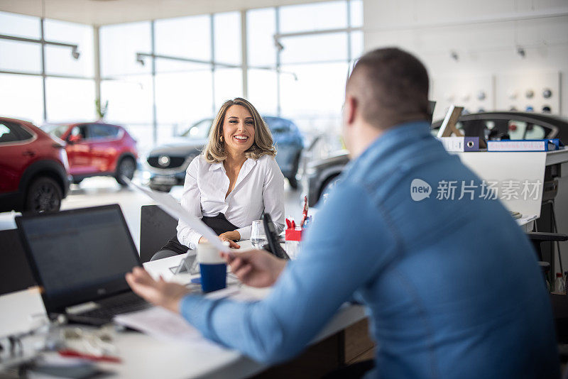 在汽车经销店，销售员与女顾客坐着聊天