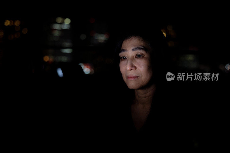 成熟的女人晚上在阳台上用智能手机