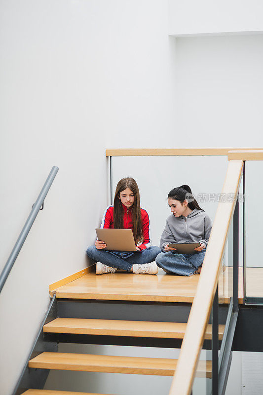 高中楼梯上的女孩们拿着笔记本和平板电脑。