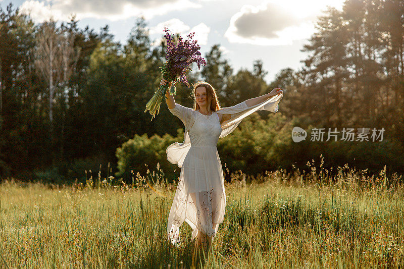 年轻美丽的女人，穿着白色的衣服，拿着鲜花在草地上跳舞。女孩喜欢自然和自由。自然美景。跳舞,运动。心理健康，没有压力，有梦想。日落。