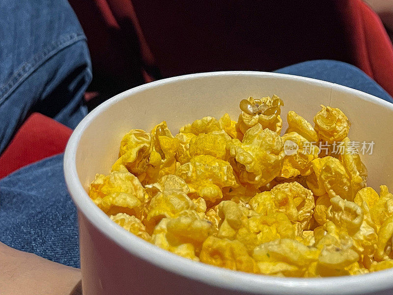 电影院的爆米花桶的特写图像，电影快餐食品桶，红色天鹅绒座椅，重点在前景