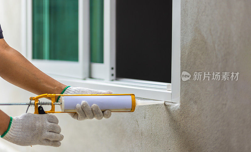建筑工人用硅酮密封胶填塞外窗框。