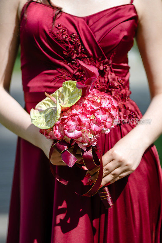 特写:一个不知名的女人，穿着红色的衣服，手里拿着红色的绣球花