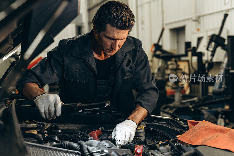 腰部肖像的汽车机械师检查和控制汽车发动机，而在车库工作。库存图片