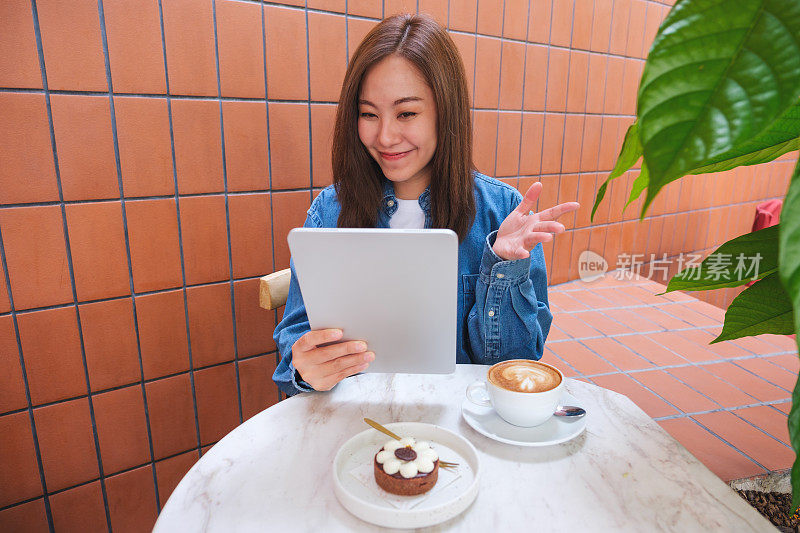 肖像图像的年轻亚洲妇女使用数字平板电脑视频通话，在线会议在咖啡馆