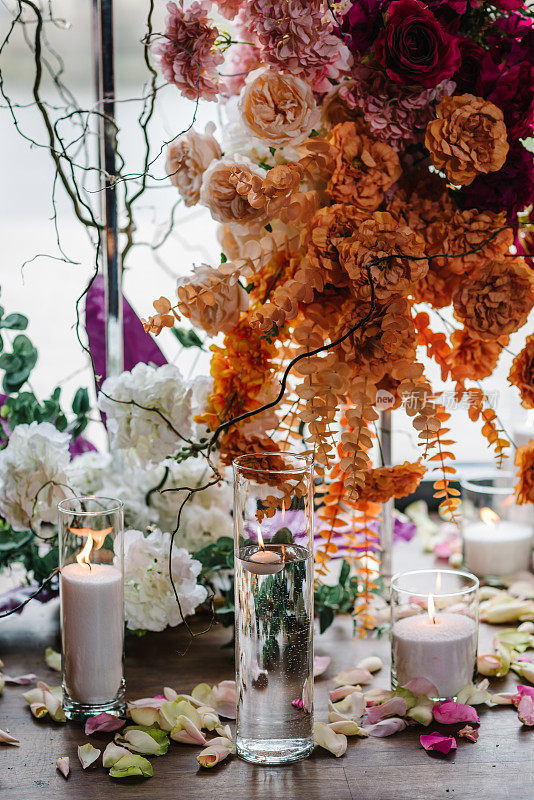 蜡烛，地上的玫瑰花瓣。特写装饰细节。照片墙，粉红色拱门装饰，宴会区，大厅生日派对橙色花朵。豪华婚礼的婚宴。活动装饰