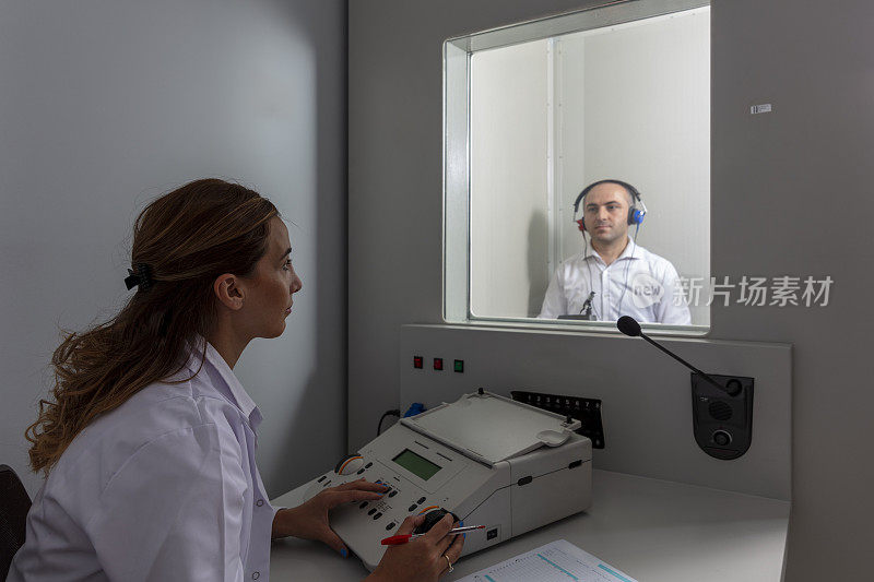 女听力学家在私人录音室用听力计对男病人进行听力检查。