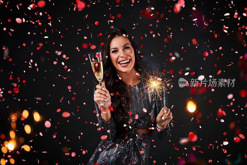 一个美丽的女人被五彩纸屑包围，手里拿着糖果和一杯香槟。新年晚会。