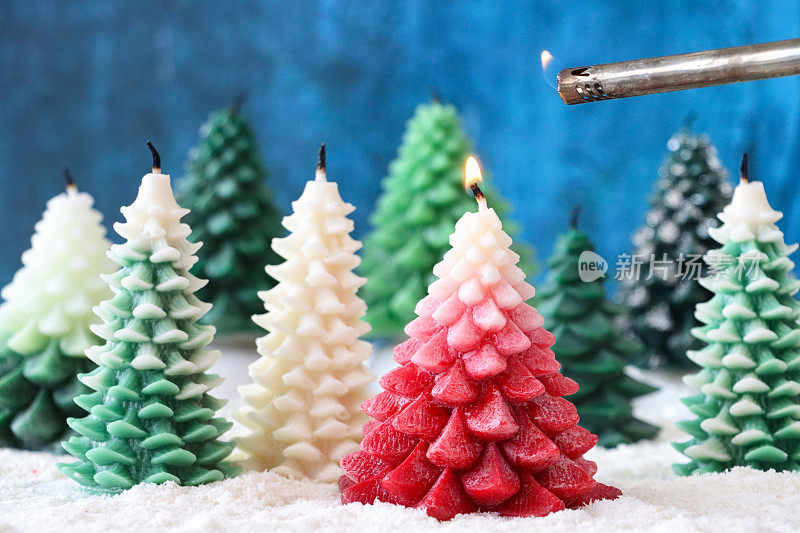 圣诞冷杉森林场景特写，一组熄灭的圣诞树蜡烛放在人造雪上，红色的蜡烛用安全气体打火机点燃，斑驳的蓝色背景，重点放在前景上
