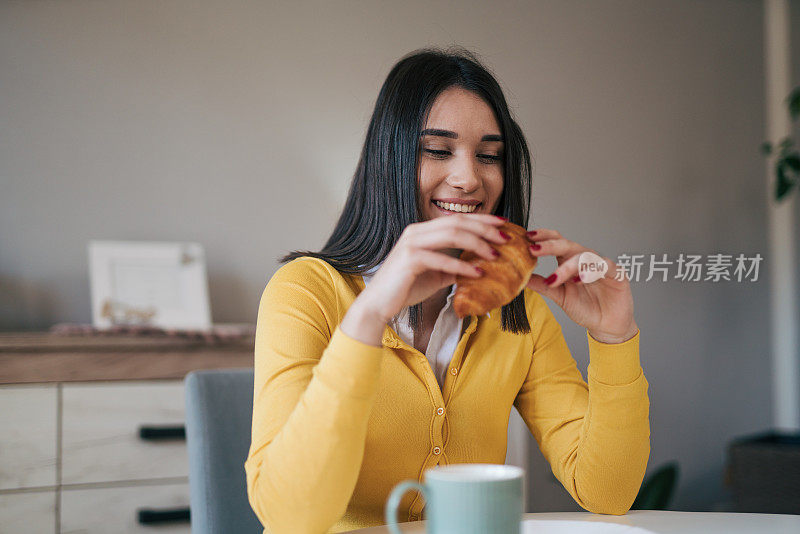 年轻女子在厨房吃牛角面包