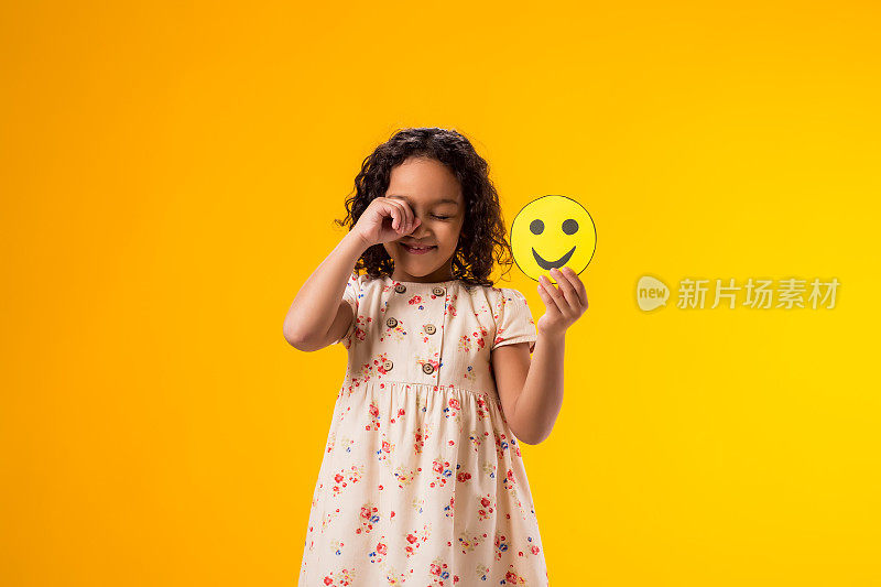 哭泣的小女孩拿着快乐的表情符号。心理健康、心理学与儿童情绪的概念