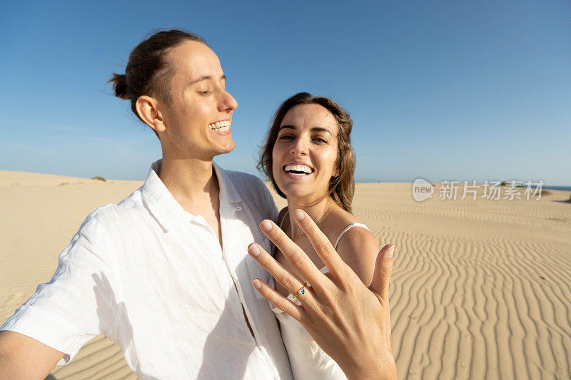 快乐的夫妇在沙漠沙滩上展示订婚戒指