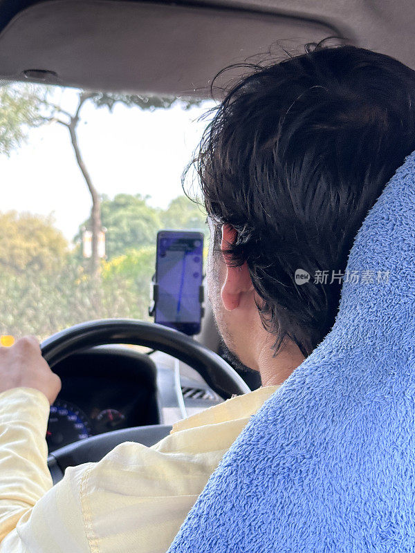 印度男子驾驶私人出租车的特写图像，使用安装在智能手机上的卫星导航，从出租车内部通过挡风玻璃看到高速公路，后视图，焦点在前景上