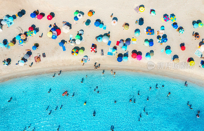 鸟瞰沙滩上五颜六色的雨伞，蓝色大海里的人们