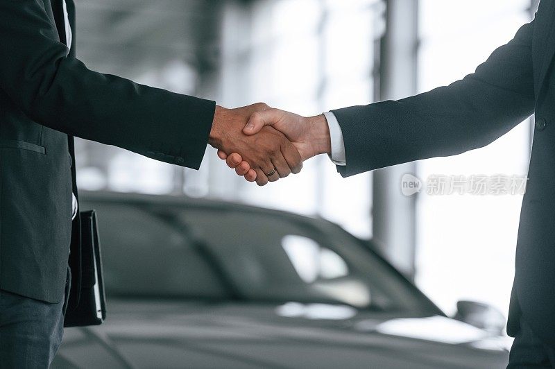 特写视图。两个商人正站在汽车展示厅里做交易，握手