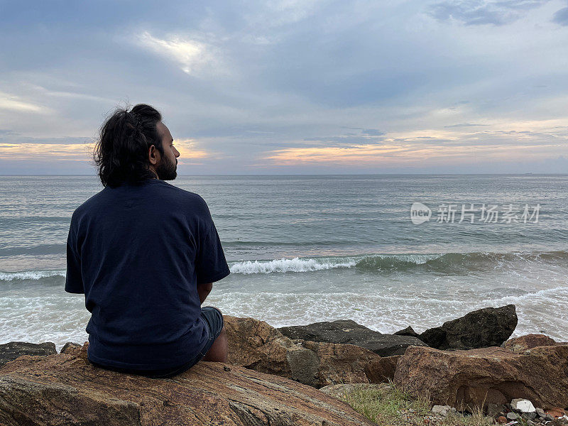 印度人坐在斯里兰卡海岸线上的人造岩石海防上的图像，海岸侵蚀抛石装甲墙，海岸管理，海洋，后视图，科伦坡，斯里兰卡