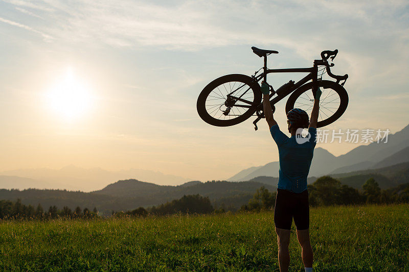 骑自行车的人把自行车举过头顶，看着日落