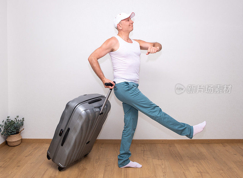 一个穿着白色t恤、戴着棒球帽的男人微笑着，大胆地提着一个大手提箱走着。准备出发。