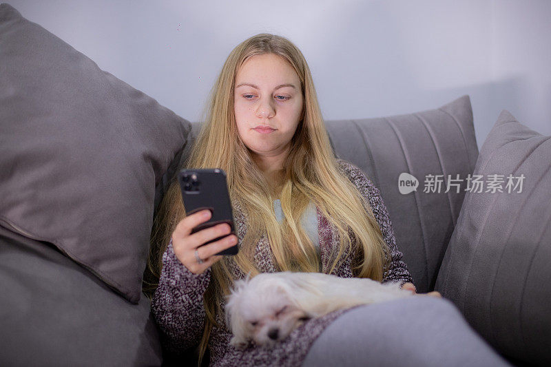 年轻女子在玩手机，而她的狗在她腿上睡觉