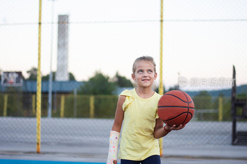 微笑的可爱小女孩的肖像，手受伤拿着篮球