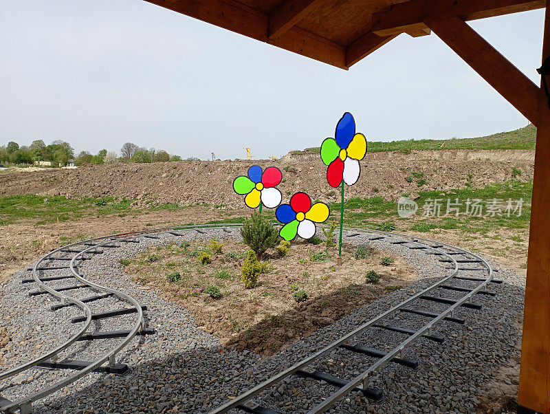 儿童铁路景点的轨道绕着五颜六色的塑料花瓣人造花转了个180度大转弯。美丽的儿童游乐园景观设计。